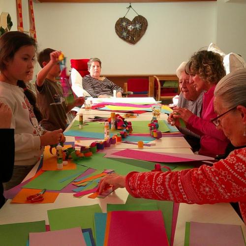 Mehrere Senioren auf der linken Seite und mehrere Kinder auf der rechten Seite eines Tisches beim Basteln