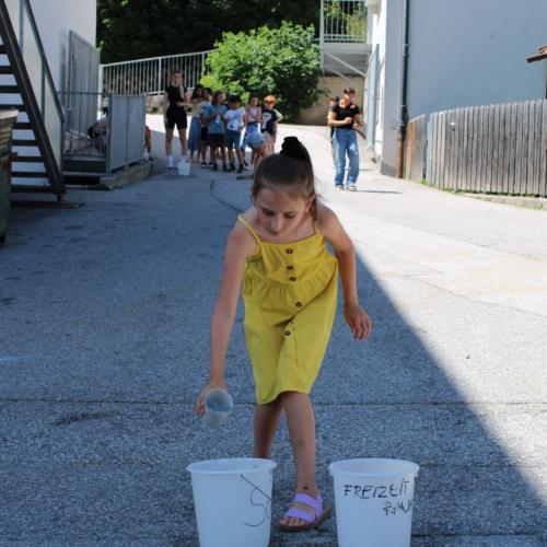 Mädchen leert einen Becher voll mit Wasser in einen Eimer 