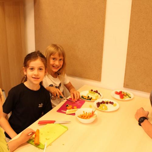 4 Kinder sitzen an einem Tisch und schneiden Obst und Gemüse 