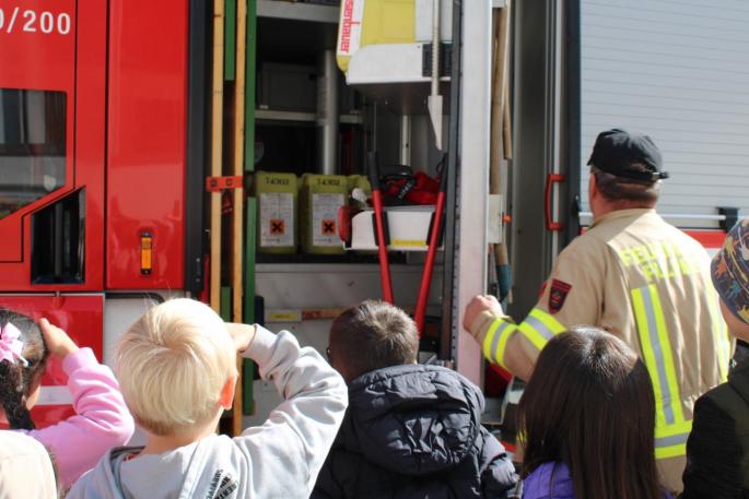 Der Feuerwehrmann erklärt den Kindern was sich im Feuerwehrauto befindet