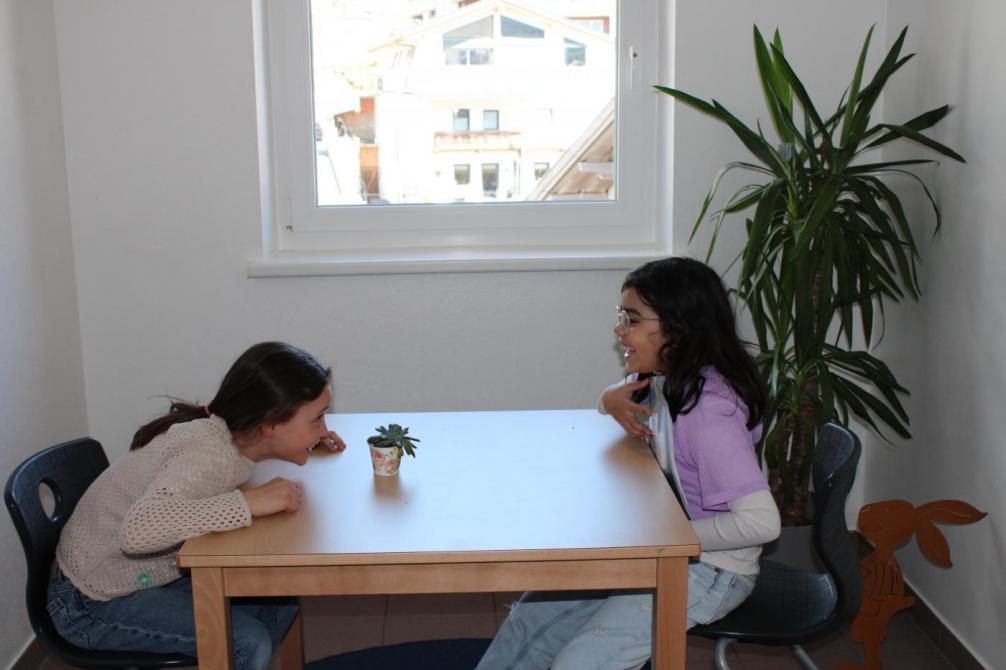 2 Mädchen im Gespräch, sitzen sich am Tisch gegenüber