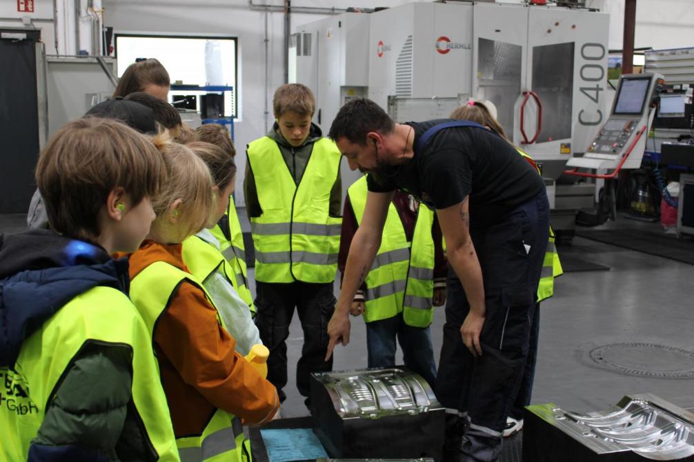 Mitarbeiter zeigt den Kindern eine Maschine 