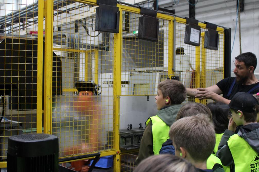 Mitarbeiter zeigt den Kindern die Arbeitsprozesse an einer Maschine 