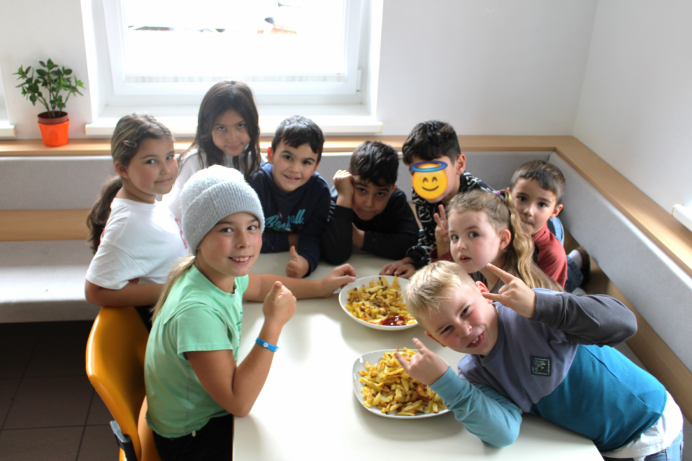 9 Kinder sitzen am Tisch mit selbstgemachten Pommes